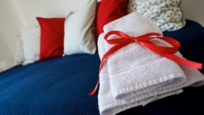 Ein ordentlich bezogenes Bett mit einer blauen Tagesdecke und weißen Kissen, eines davon rot.