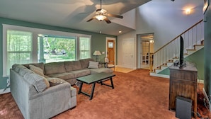 A living room with a sectional sofa, a coffee table, and a ceiling fan. There is a staircase with a wooden railing leading to another room. - Spacious Downtown Chico Home ~ Half Mile to CSU! (Chico)