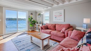 Una sala de estar acogedora con un gran ventanal con vistas a un lago, un sofá a rayas, una mesa de centro de madera y una estantería.