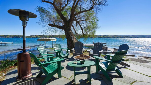 Un patio junto al lago con sillas Adirondack, una fogata y una mesa.