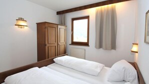 Ein Hotelzimmer mit zwei Einzelbetten, einem Holzschrank und einem fensterbepflanzten Fenster.