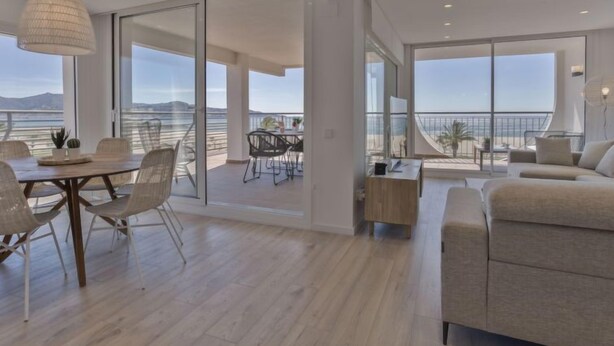 Un salon moderne doté d’une grande fenêtre, d’un coin repas et d’un balcon offrant une vue sur la mer.