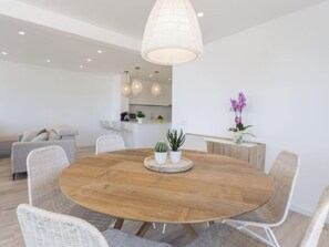 Un comedor moderno con una mesa redonda de madera, sillas de mimbre y una isla central con plantas.