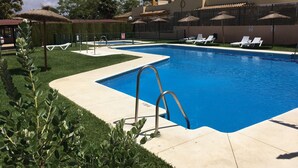 Una piscina con agua cristalina azul, rodeada de un césped cuidado y algunas tumbonas.