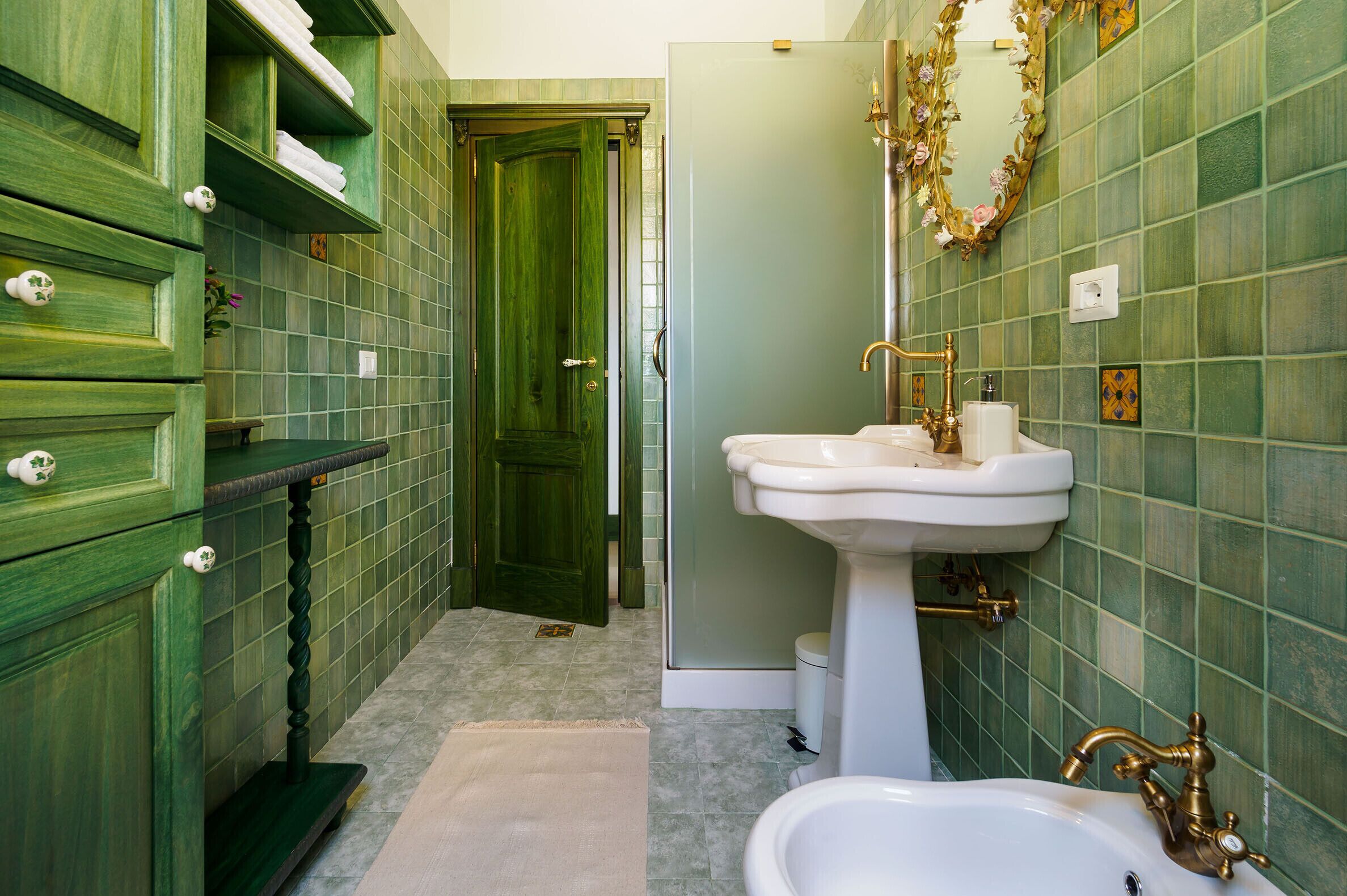 Ein Badezimmer mit grünen Schränken, einem weißen Waschbecken mit goldfarbenen Armaturen und einer grünen Tür.