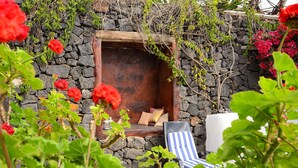 A stone wall, a wooden bench with cushions, and a blue-striped lounge chair. - La Bodega – On a Volcano with Piano, Sea Views, Private Terrace & Wi-Fi (Haria)
