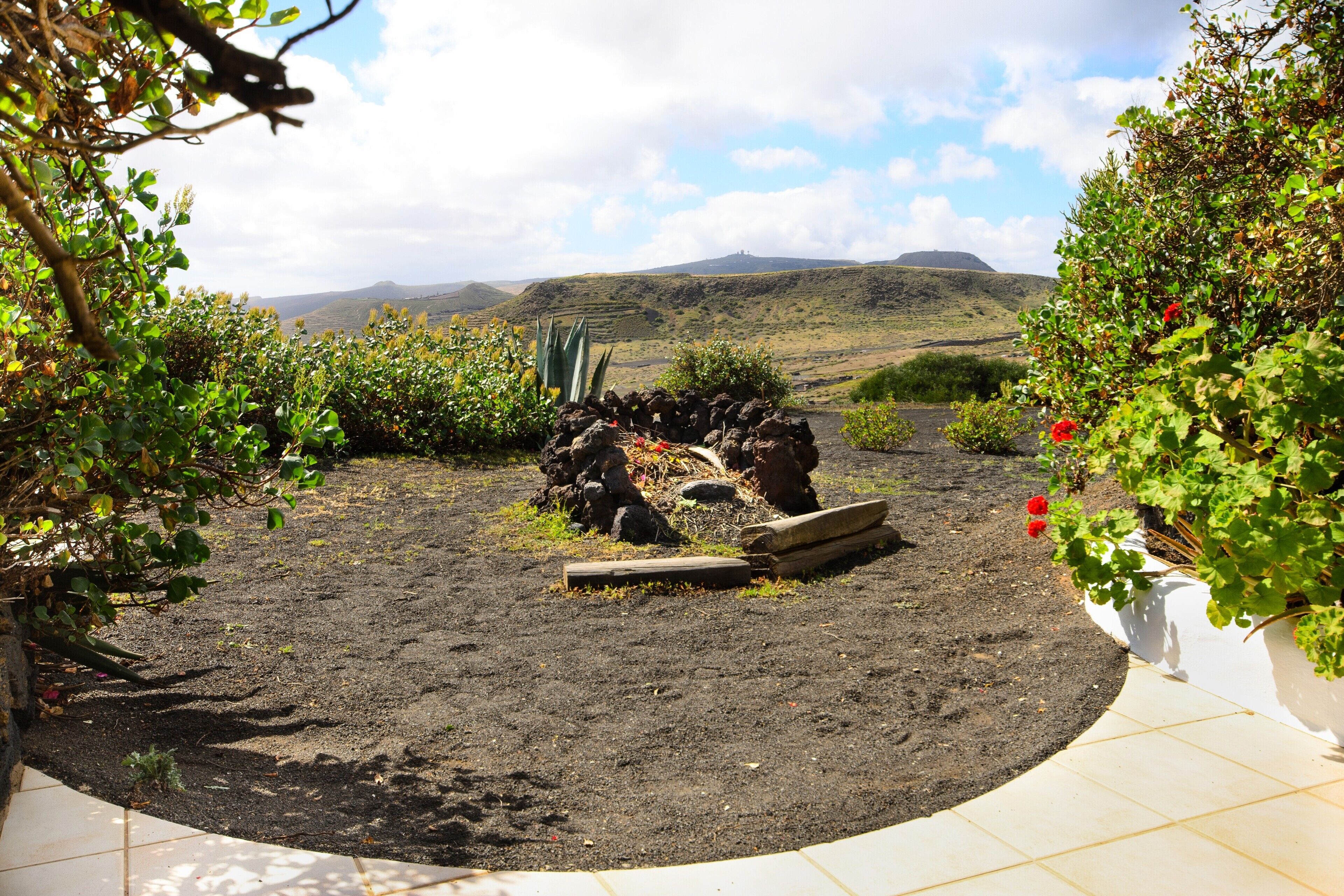 Un jardín con muro de piedra, plantas y vistas a colinas distantes.