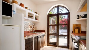 A kitchen with a tiled backsplash, a refrigerator, a stove, and a door leading outside. - La Bodega – On a Volcano with Piano, Sea Views, Private Terrace & Wi-Fi (Haria)
