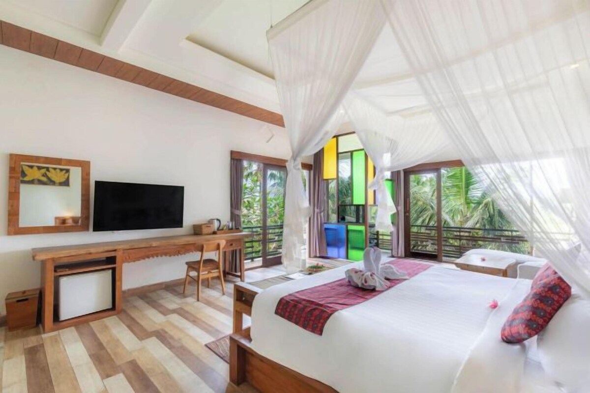 A bedroom with a bed, a desk, a TV, and a balcony with a view of greenery.