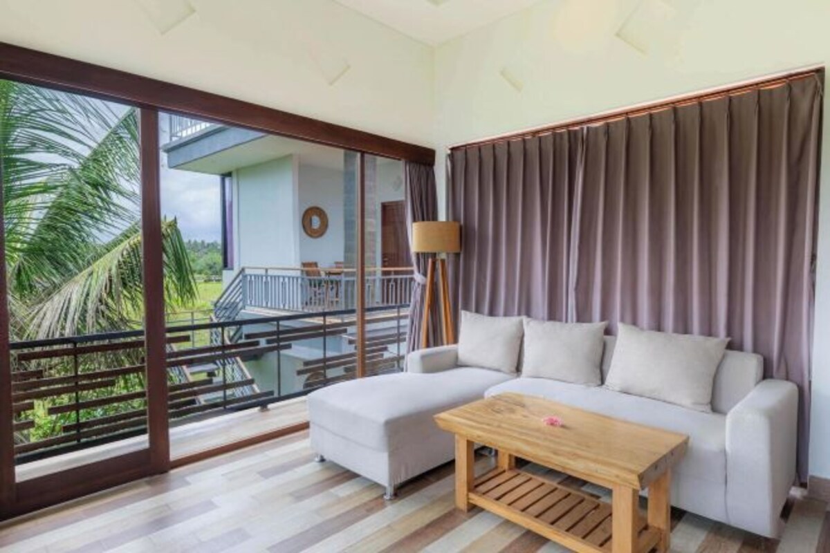 Un salon moderne avec un canapé, une table basse en bois et une vue sur un balcon agrémenté de palmiers.