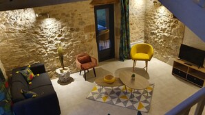 A cozy living room with a stone wall, a sofa, a yellow armchair, a coffee table, and a TV stand. - Stone country house (Saint-Remy)