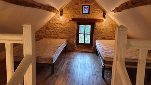 A cozy attic bedroom with two bunk beds, wooden beams, a stone wall, and a small window with a stained glass design. - Stone country house (Saint-Remy)