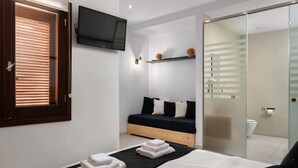 Um quarto moderno com uma cama, uma TV fixada na parede, uma mesa de cabeceira e uma porta de correr para um banheiro.