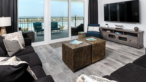 Una sala moderna con un sofá, dos mesas de centro, un televisor y un balcón con mobiliario exterior.