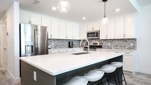 Cocina moderna con armarios blancos, un refrigerador de acero inoxidable, un microondas y una isla grande con taburetes de bar.