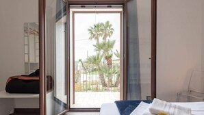 A bedroom with a bed, a bench, and a view of palm trees through a glass door. - Modica Country Villa - Villa with pool (Modica)