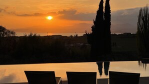 A sunset view from an infinity pool with three lounge chairs.