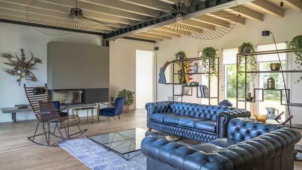 A modern living room with a leather sofa, a rocking chair, and a glass coffee table. There are potted plants and a bookshelf with decorative items. - Charming rental villa, magnificent views of Lake Garda, park and private pool (Lazise)