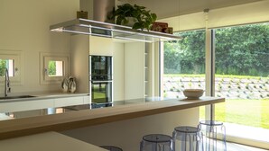 A modern kitchen with a large island, stainless steel appliances, and a view of a garden through large windows.