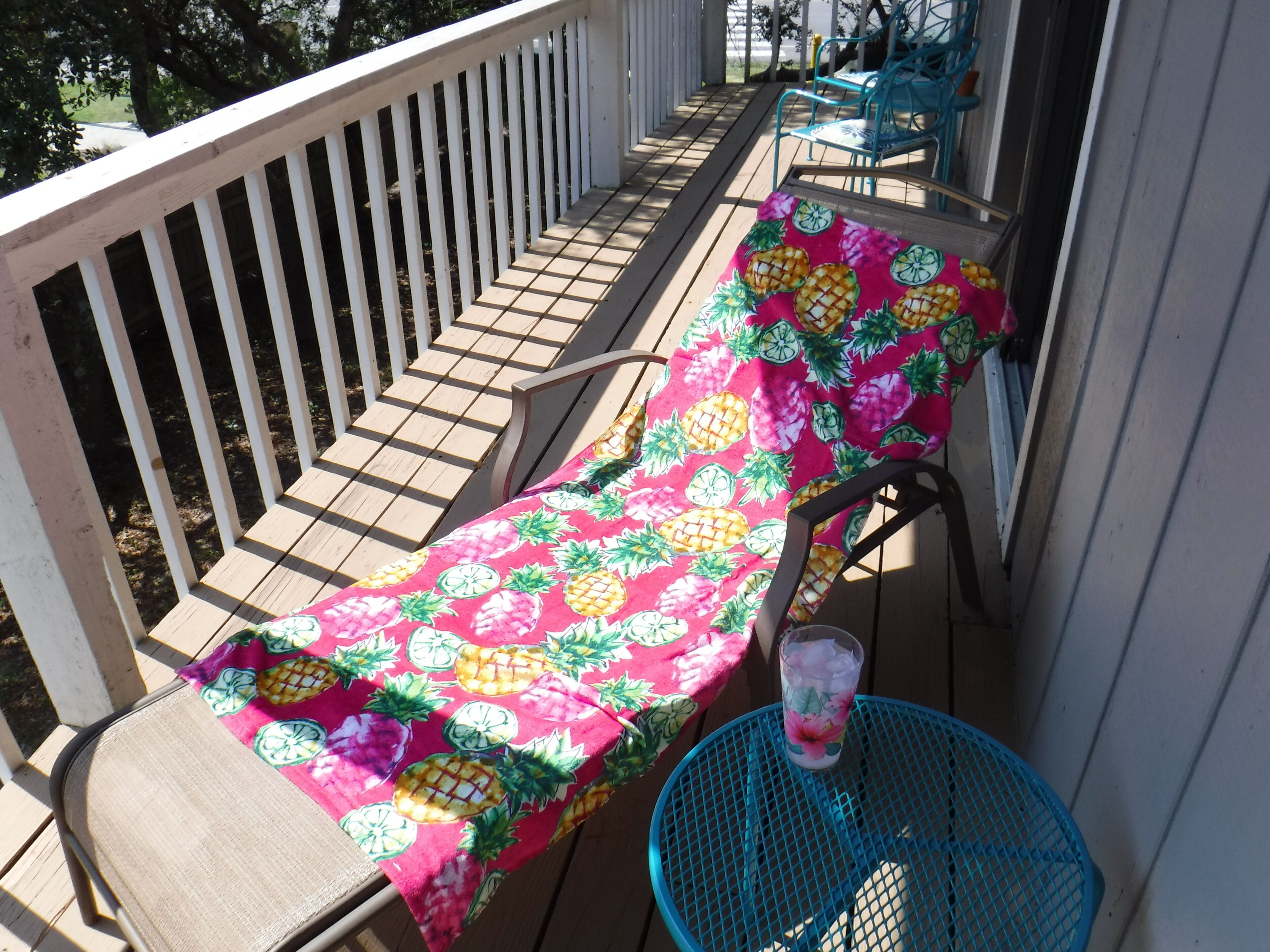 A wooden deck with a table covered in a pineapple-patterned tablecloth and a chair.