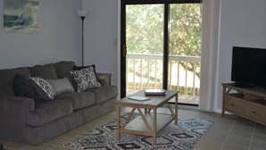 Un salon comprenant un canapé, une table basse, un meuble pour la télévision et une vue sur l’extérieur, accessible par une porte-fenêtre coulissante.