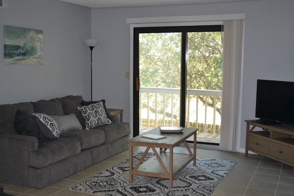 A living room with a sofa, coffee table, TV stand, and a view through a sliding glass door.
