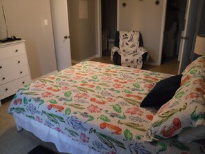 A bedroom with a floral-patterned bedspread, a white dresser, and a chair.