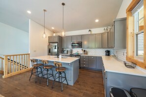 A modern kitchen with a central island, bar stools, and a wooden staircase. - I'm Your Huckleberry at Lake Chelan Lookout Vacation Rentals (Chelan)