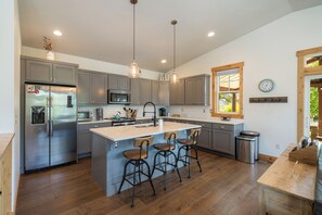 A modern kitchen with stainless steel appliances, a central island with bar stools, and a large window providing natural light. - I'm Your Huckleberry at Lake Chelan Lookout Vacation Rentals (Chelan)