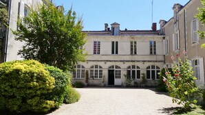 A courtyard with a gravel path leading to a building with arched windows and a central door. - Le Gite du parc 2 rooms parking, quiet 2 steps from the old port and the beach (la rochelle)