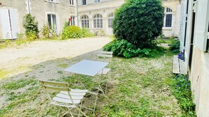A courtyard with a small table and chairs, surrounded by greenery and a building with multiple windows and balconies. - Le Gite du parc 2 rooms parking, quiet 2 steps from the old port and the beach (la rochelle)
