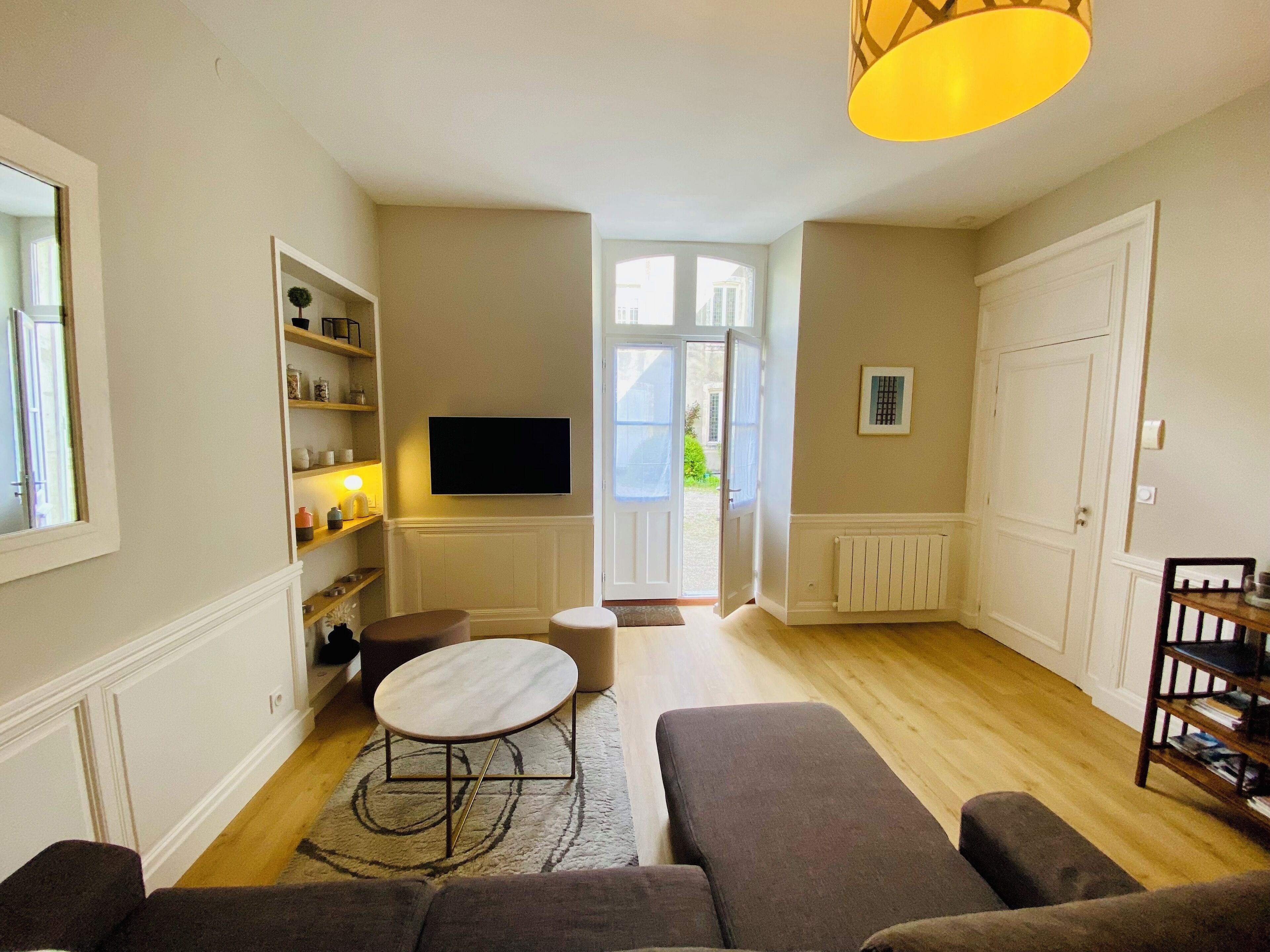 A living room with a sofa set, a coffee table, a TV mounted on the wall, and a bookshelf.