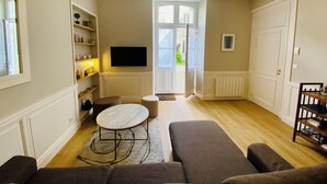 A living room with a sofa set, a coffee table, a TV mounted on the wall, and a bookshelf. - Le Gite du parc 2 rooms parking, quiet 2 steps from the old port and the beach (la rochelle)