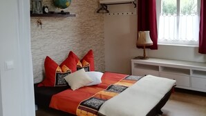 Un dormitori amb un llit, una tauleta de nit, una làmpada, un globus terràqui, un rellotge i una finestra amb cortines.