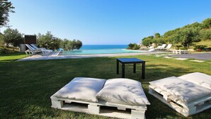 A poolside area with lounge chairs and a small table, overlooking a clear blue ocean. - Modern Villa with Private Golf Practice, Pool, Garden, Terrace, Wi-Fi, Sea View (Campofelice di Roccella)