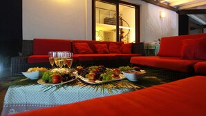 A dining area with a red sofa, a table set with food and drinks, and a view of the interior through a glass door. - Modern Villa with Private Golf Practice, Pool, Garden, Terrace, Wi-Fi, Sea View (Campofelice di Roccella)