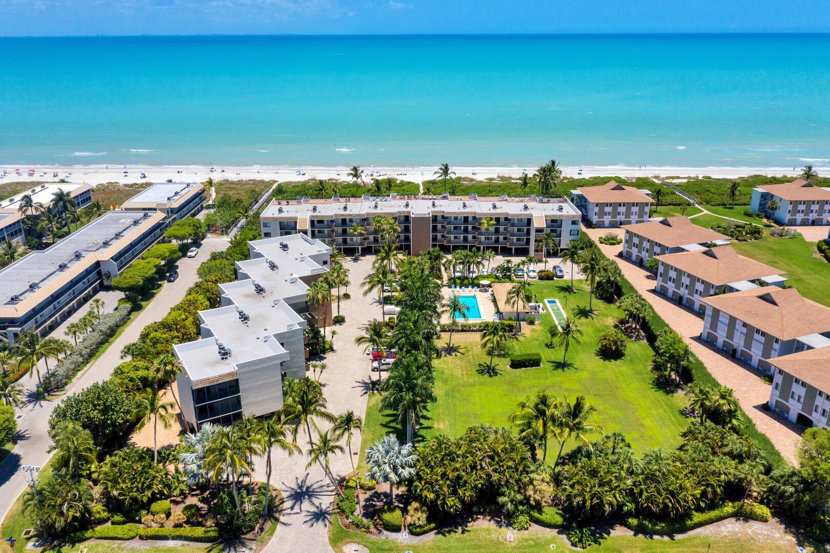 Un resort con varias edificaciones, una piscina central y vista al mar.