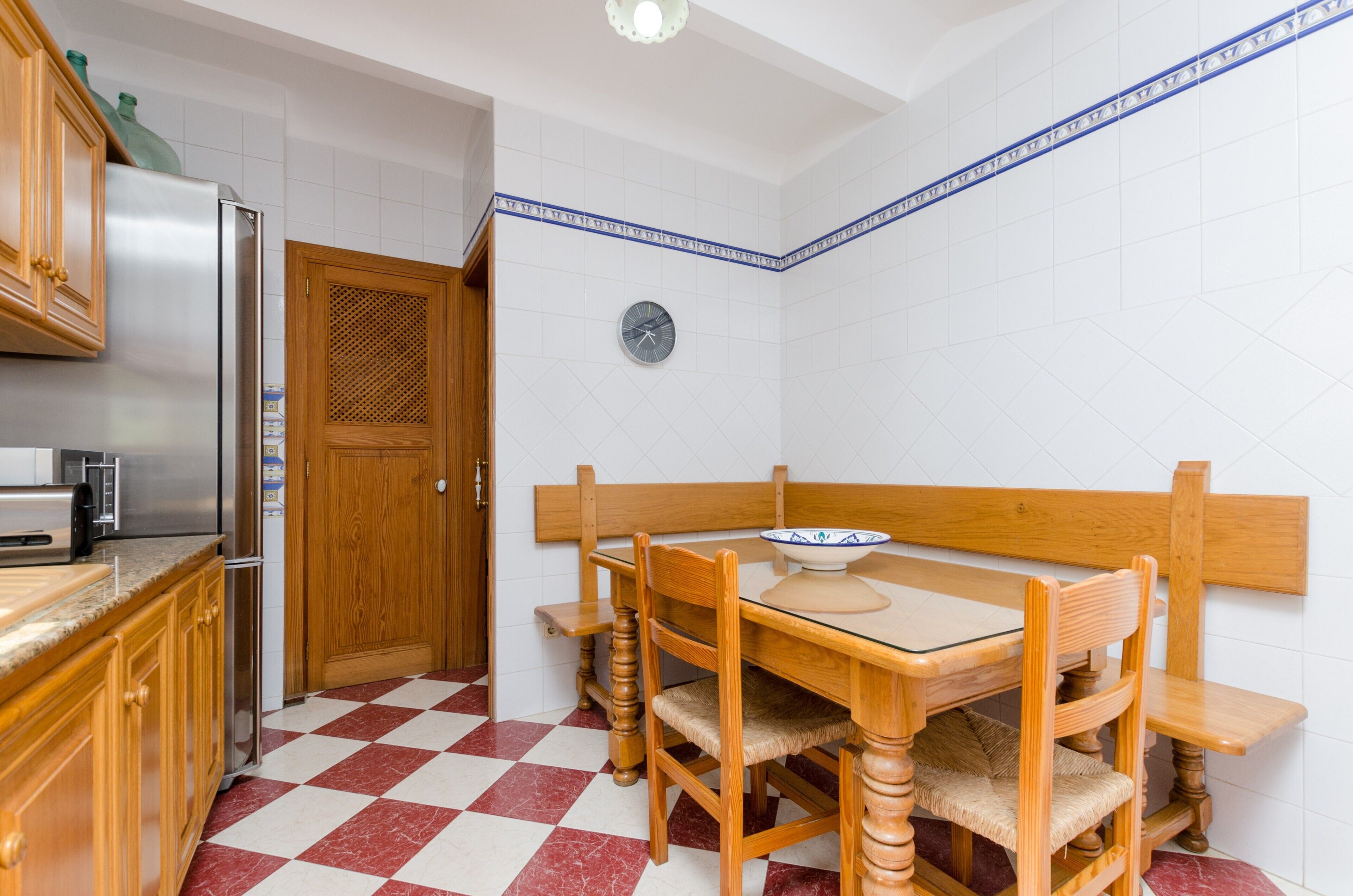A kitchen with a checkered floor, wooden cabinets, a refrigerator, a sink, and a dining table with chairs.