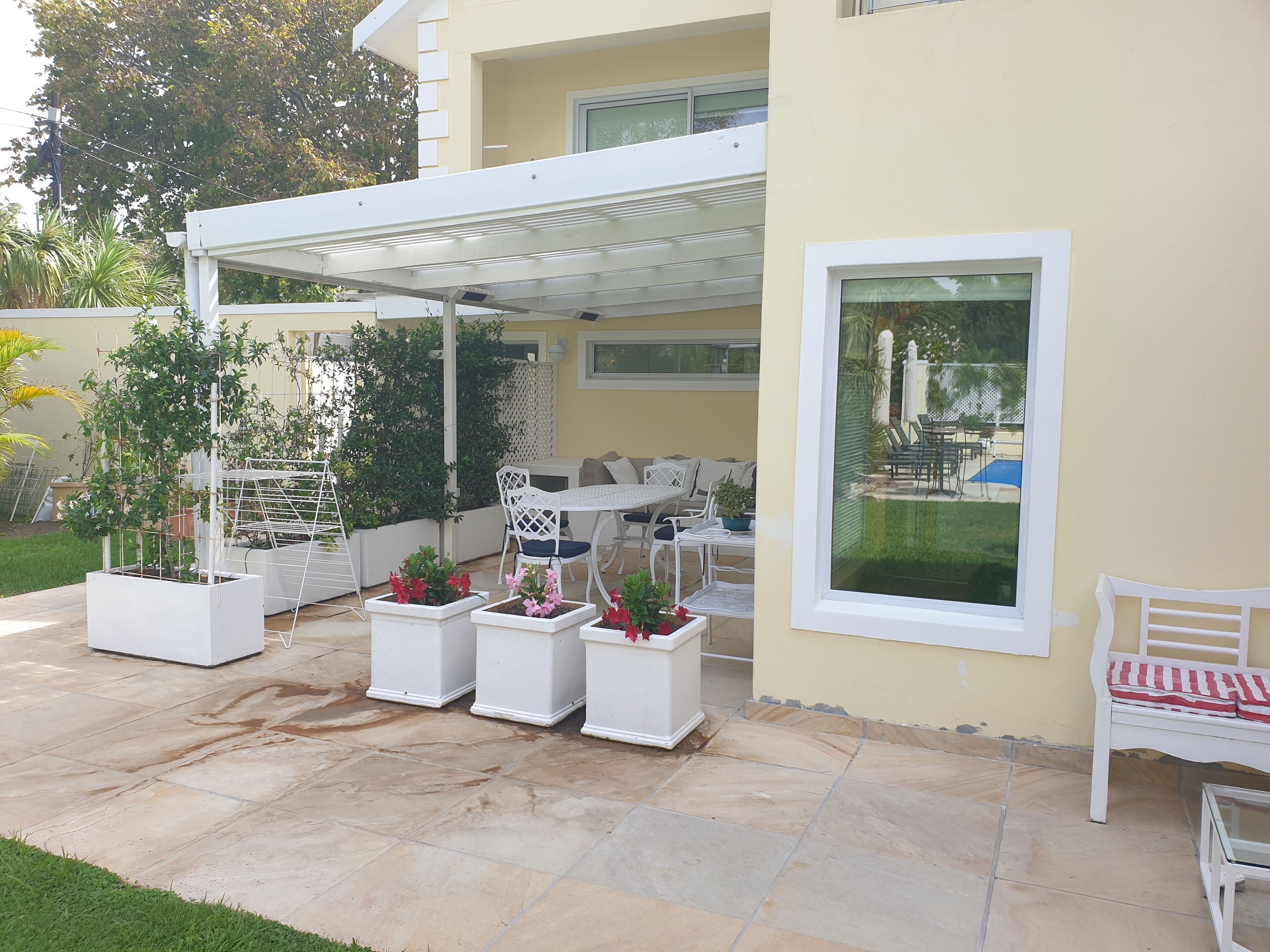 Un patio coperto con mobili da esterno, piante in vaso e vista su una piscina.