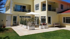 A two-story building with a flat roof, large windows, and a covered patio area with potted plants and outdoor furniture. - 4-STAR-Apartment (AA Superior rated) at the Constantia Wine Route / Kapstad (Constantia)