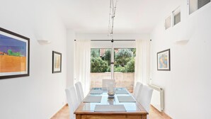 A dining area with a glass table, white chairs, and a view of greenery outside. - Fantastic villa with pool in Betlem (Arta Betlem)
