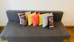 A grey sofa with five pillows in various colors and patterns. - Rent studio per week (Eaux-Vives)