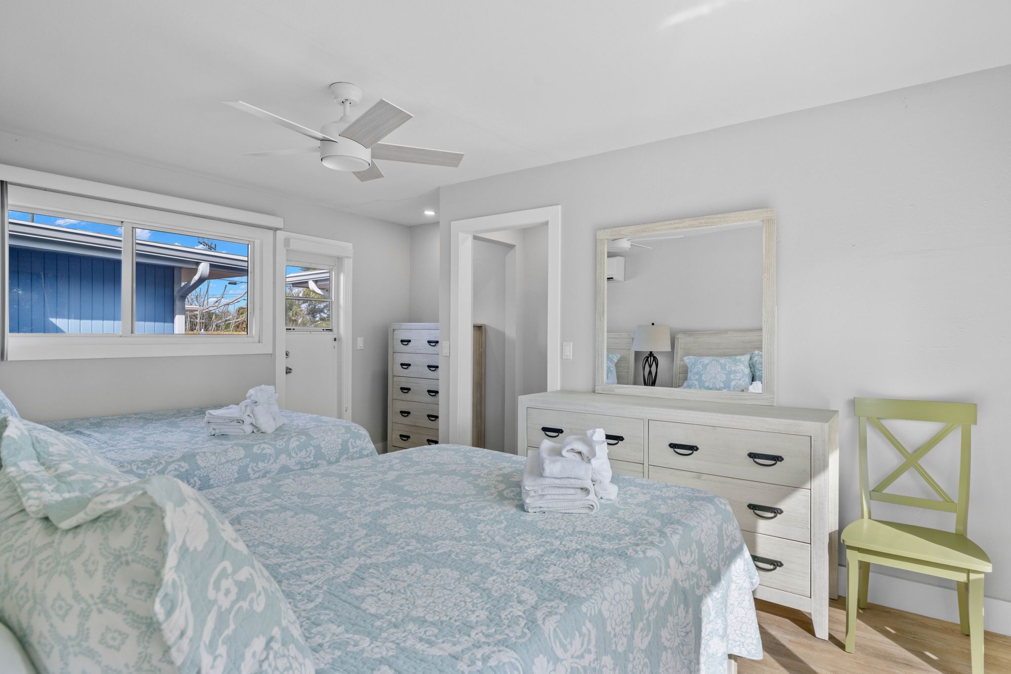 A bedroom with two beds, a dresser, a mirror, and a ceiling fan.