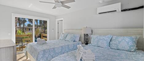 A hotel room with two beds, a ceiling fan, an air conditioning unit, a lamp, and a view of the outdoors.