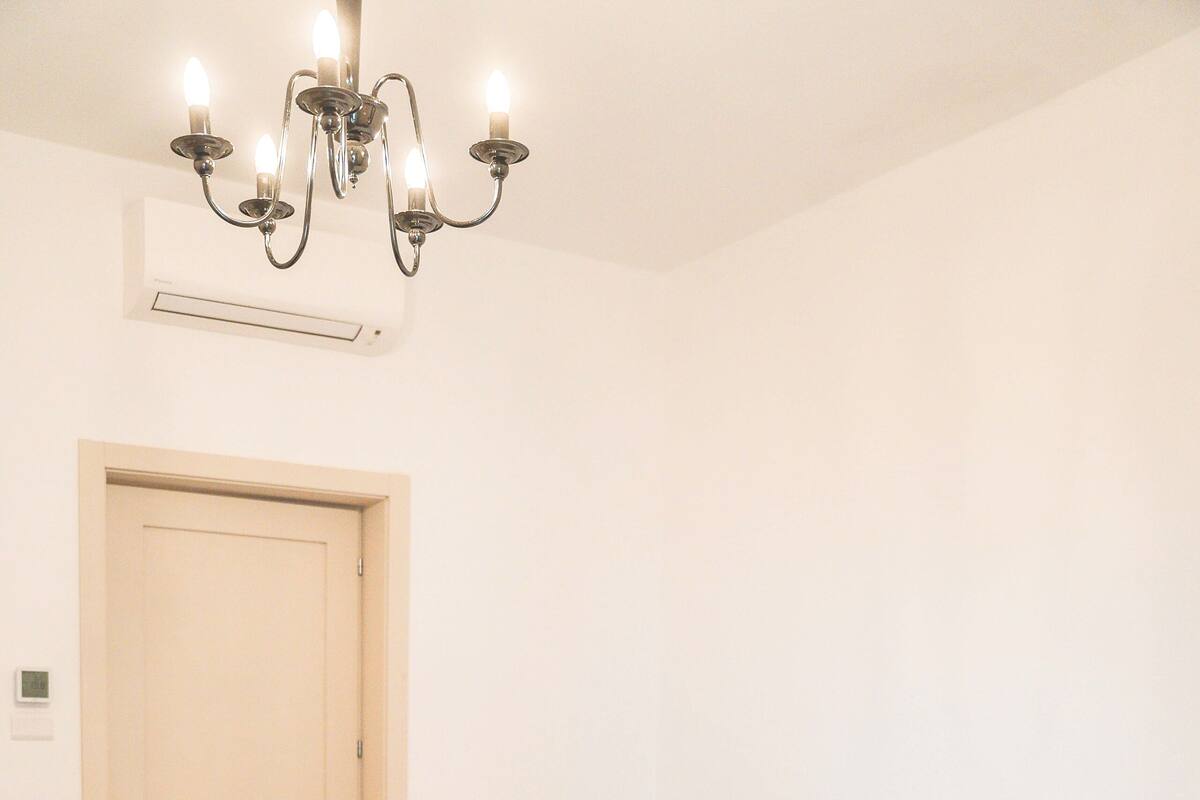 Une chambre à coucher avec un grand lit, un plancher en bois, un lustre, une table de chevet avec une lampe et une porte.