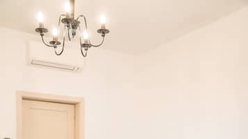 Un dormitorio con una cama grande, suelo de madera, candelabro, mesita de noche con lámpara y una puerta.