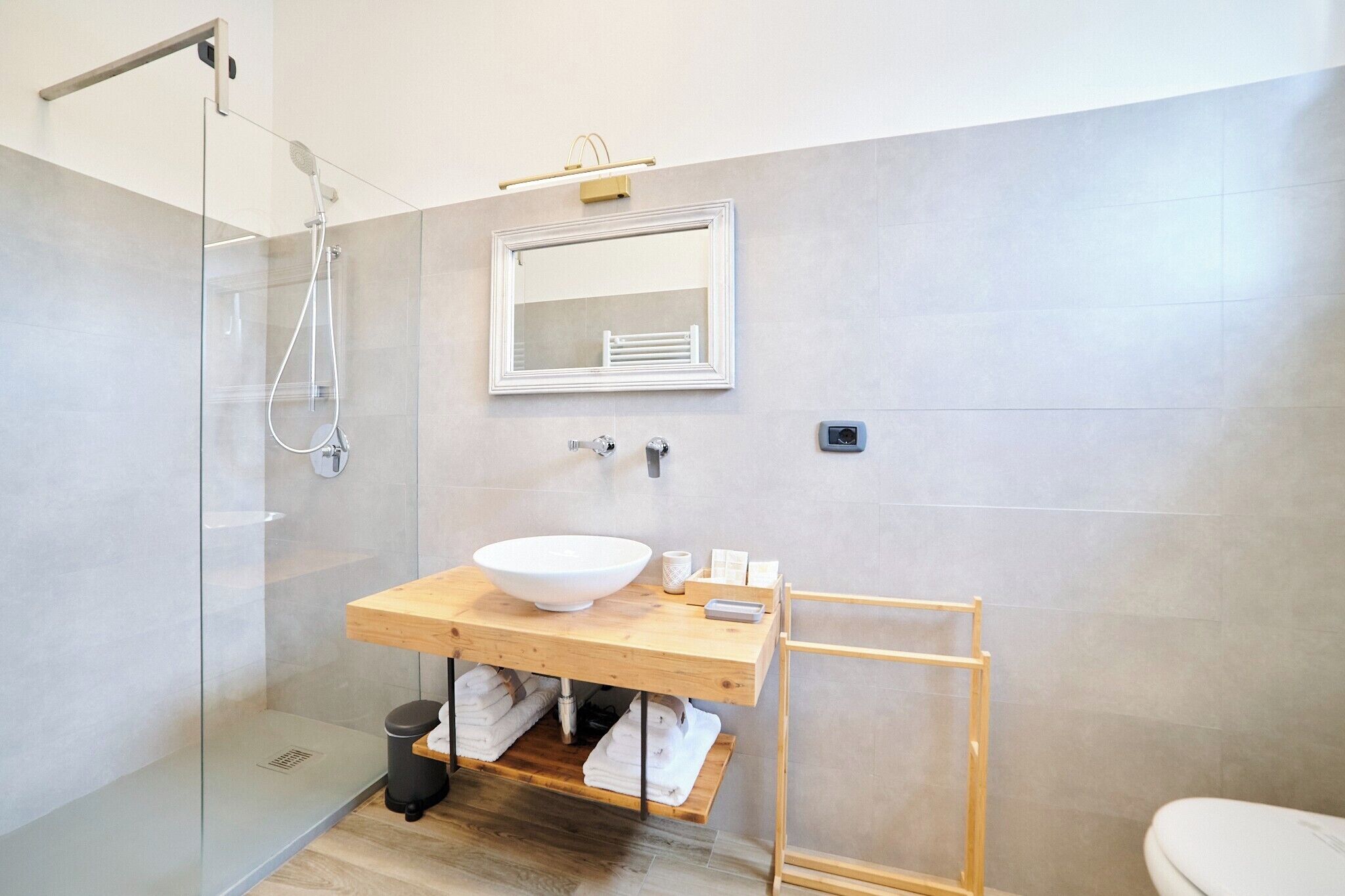 Une salle de bain moderne avec une douche à parois de verre, un meuble-lavabo en bois doté d’un grand évier et un miroir au-dessus.