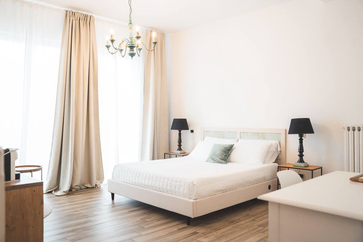 Une chambre à coucher avec un grand lit, deux tables de chevet avec des lampes, un plancher en bois et un lustre.