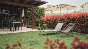 Eine Terrasse mit einer Pergola, Sitzgelegenheiten im Freien und einem Garten mit roten Blättern.