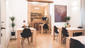 Ein moderner Essbereich mit Holztischen und schwarzen Stühlen, eine Bar mit Weinflaschen und ein großes Gemälde an der Wand.
